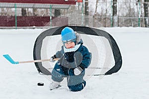 Little funny boy with her mother skating in the park. Play ice hockey with stick and goal. Outdoor. Winter sport