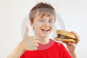 Little funny boy in a red shirt recommends and likes tasty hamburger on white background