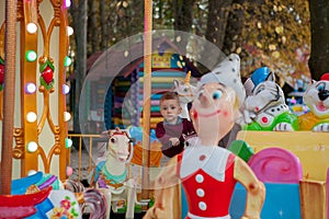 Little funny boy riding on the horse is a roundabout carousel in an amusement park. Happy child, having fun outdoors on a sunny da