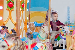 Little funny boy riding on the horse is a roundabout carousel in an amusement park. Happy child, having fun outdoors on a sunny da