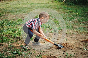 Little funny boy with shovel in garden