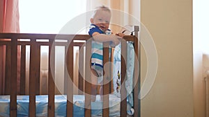 Little funny boy standing in baby bed and laughing. Smiling adorable child on feet in playpen. Happy childhood concept.