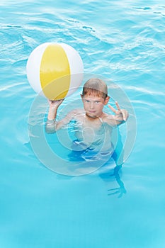 Little funny boy in the swimming pool with ball