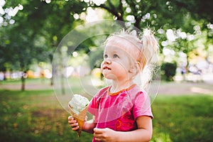 Little funny girl blonde eating sweet blue ice cream in a waffle cup on a green summer background in the park. smeared her face an