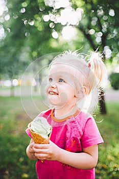 Little funny girl blonde eating sweet blue ice cream in a waffle cup on a green summer background in the park. smeared her face an
