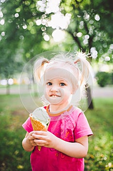 Little funny girl blonde eating sweet blue ice cream in a waffle cup on a green summer background in the park. smeared her face an