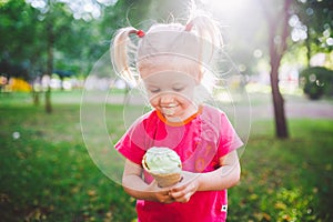 Little funny girl blonde eating sweet blue ice cream in a waffle cup on a green summer background in the park. smeared her face an