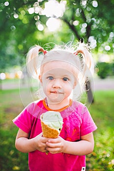 Little funny girl blonde eating sweet blue ice cream in a waffle cup on a green summer background in the park. smeared her face an