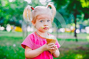 Little funny girl blonde eating sweet blue ice cream in a waffle cup on a green summer background in the park. smeared her face an