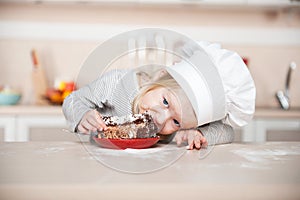 Little funny girl with chef hat eating cake