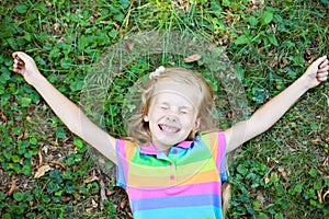 Little funny girl with closed eye lying on grass