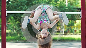 Little funny girl hanging upside down on the horizontal bar. slow motion