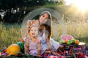 Little funny girl with her mother on a summer picnic with fruit and watermelon
