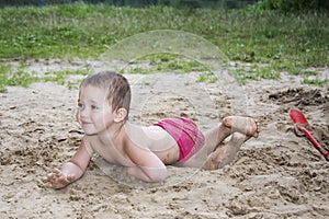 Little funny girl lying on the sand near the lake in summer and
