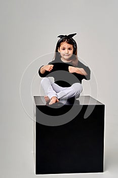 little funny girl sitting on a black cube on a white background