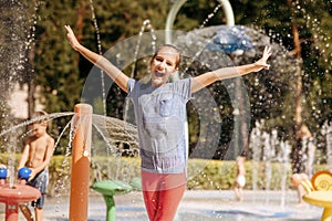 Little funny girl in splashes on water playground