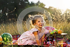 Little funny girl on a summer picnic with fruit and watermelon