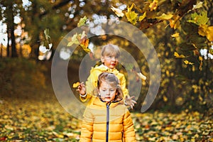 Little funny girls, sisters in stylish yellow raincoat, jacket play in autumn forest or park outdoors, throw up above head old