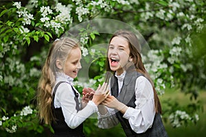 Little funny girls in stylish school uniforms play outdoors in the blossoming apple park