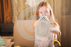 Little funny housewife with iron. Iron in the hand of the girl on the Ironing Board irons and steams clothes. Little girl playing