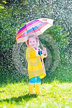 Little funny toddler with umbrella playing in rain