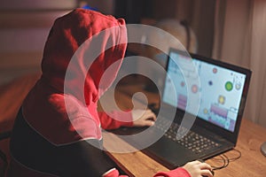 Little gamer kid in hood playing mass multiplayer game online on laptop