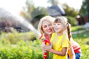 Little gardener girl with mother watering on lawn near house