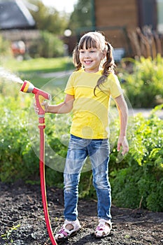 Little gardener girl watering with hosepipe photo