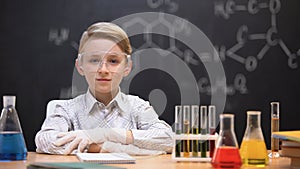 Little genius sitting in protective glasses, chemical liquids in tubes on table