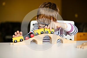 Little ginger child boy in the glasses with syndrome dawn playing with wooden railways