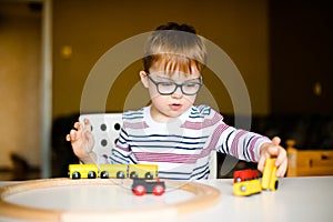 Little ginger child boy in the glasses with syndrome dawn playing with wooden railways