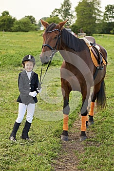 Little gir jockeyl lead horse by its reins across country in professional outfit