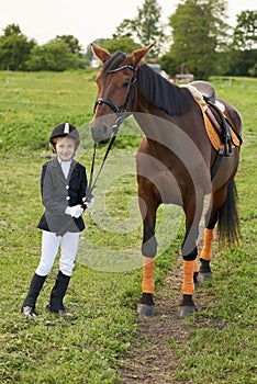 Little gir jockeyl lead horse by its reins across country in professional outfit photo