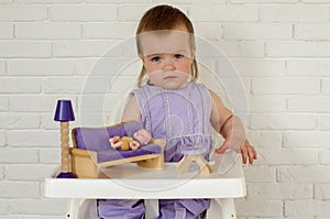 Little girl 1 years playing with doll house furniture. Cute baby girl in violet dress. Violet style