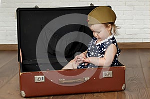 Little girl 1 years in soviet military cap and polka dot dress. Retro suitcase