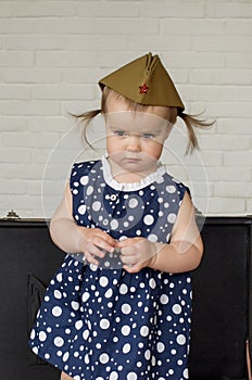 Little girl 1 years in soviet military cap and polka dot dress. Retro suitcase