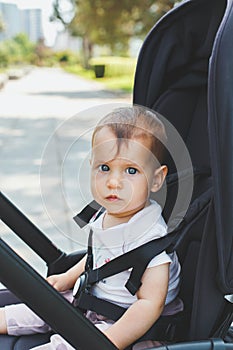 a little girl 10 months old sits in a black stroller in the park