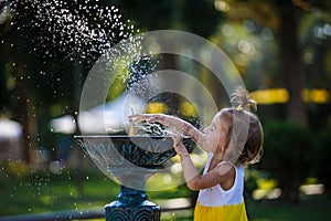 A little girl of 3 years old plays on the street with a stream of drinking fountain and enjoys the spray.