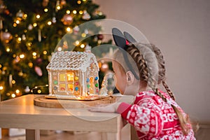 a little girl of about 4-5 years old looking at a gingerbread house with sweets against the background of a Christmas