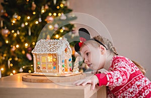 a little girl of about 4-5 years old looking at a gingerbread house with sweets against the background of a Christmas