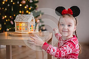 a little girl of about 4-5 years old looking at a gingerbread house with sweets against the background of a Christmas
