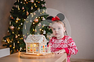 a little girl of about 4-5 years old looking at a gingerbread house with sweets against the background of a Christmas