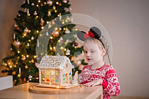 a little girl of about 4-5 years old looking at a gingerbread house with sweets against the background of a Christmas