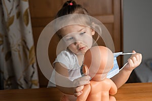 a little girl of 4 years old plays with a baby doll at home, puts a medical mask on a doll