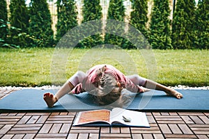 Little girl 5-6 years old lying in the Turtle pose or Kurmasana while practicing yoga outdoors