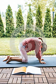 Little girl 5-6 years old standing in Marjariasana or Cat pose while practicing yoga outdoors