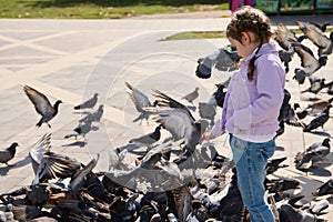 Little girl 5 years old, feeds flock of flying pigeons in town square. The concept of care and kindness for wild animals