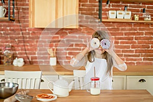 Little girl 7 years old eating donuts and drinking milk on the kitchen at home. Tasty food for kids. Homemade food concept