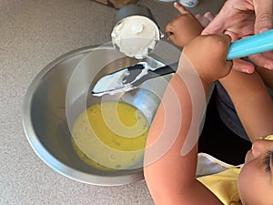 Little Girl Adding Sour Cream to Batter While Baking with Parents