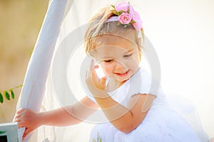 Little girl adjusts her hair of hut for games. Child with beautiful hairstyle in white dress.